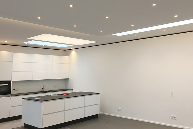 Galerie Spanndecken Küche weiss matt Gewebe mit einigen Einbaustrahlern und Lichtdeckenfeld über der Kochinsel als Arbeitslicht